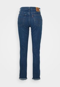 Blue denim jeans with a straight leg design, featuring a leather tag at the back and rolled cuffs, and classic back pockets with stitching.