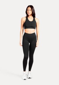 Reggiseno sportivo nero e leggings a vita alta in tessuto elasticizzato. L'outfit presenta un design aderente e uno stile minimalista, abbinato a sneakers bianche.