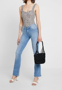 Bodysuit de estampado de leopardo con tirantes con volantes, jeans acampanados de cielo claro, sandalias de tacón bloque blanco y un bolso tejido negro.