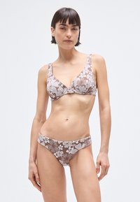 Bikini floral marrón con patrones de flores blancas. La parte superior tiene tirantes gruesos y un escote pronunciado; la parte inferior es de talle bajo con bandas anchas a los lados.