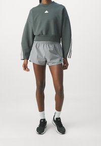 Grå kortärmad sweatshirt med vitt logo, parat med ljusgrå träningsshorts. Svarta löparskor och vita strumpor fullbordar outfiten.
