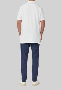 Biała koszulka polo z klasycznym kołnierzykiem i krótkimi rękawami, w połączeniu z granatowymi spodniami i białymi trampkami. Prosty, casualowy look.