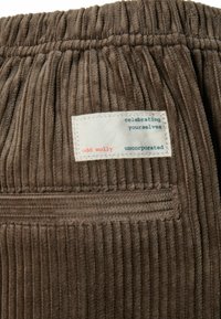 Barna kordbársony anyag, függőleges bordázattal, melyen egy fehér címke látható kék és piros felirattal: “odd molly” és egyéb részletek.