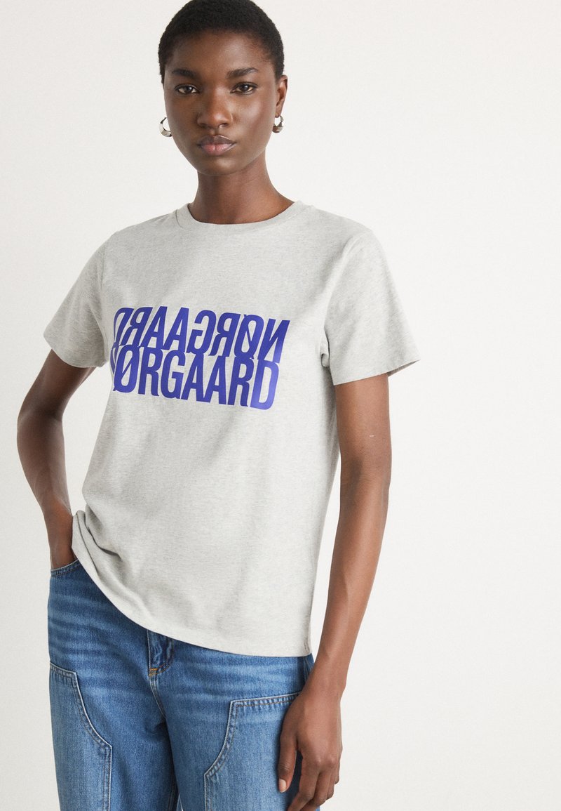 Gray cotton t-shirt with short sleeves, featuring bold blue printed text "NORGAARD" across the front, complementing straight blue jeans.