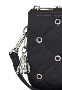 Czarna, pikowana torebka wykonana z nylonu, z metalowymi elementami, nitami oraz metalowym urokiem w kształcie misia przypiętym do paska.