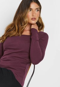 Pitkähihaoinen paita syvässä purppurassa, jossa on suora pääntie ja istuva siluetti. Valmistettu pehmeästä kankaasta, jolla on sileä rakenne.