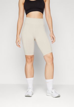 Beige høytlivs sykkelshorts laget av et elastisk stoff, med en ribbet midje og knelange ben. Kombinert med hvite joggesko og sokker.