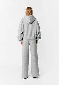 Sudadera gris con capucha y pantalones de chándal de pierna ancha a juego, hechos de un tejido suave y texturizado. Presenta una capucha y un corte holgado, ideal para el uso casual.
