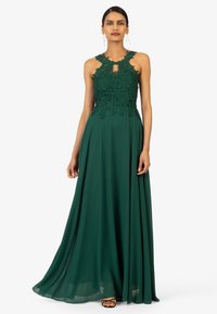 Groene avondjurk met een aansluitend kanten lijfje met bloemenpatronen, een keyhole-halslijn en een vloeiende chiffon rok. Geaccentueerd met bandsandalen.