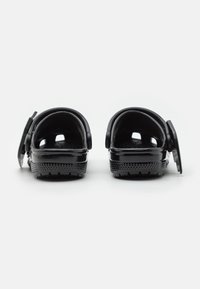 Sandales en slide noires avec une finition brillante, une sangle réglable, une semelle intérieure texturée et une semelle crantée pour l'adhérence. Vue de dos mettant en valeur les détails de design.