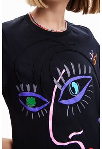 Czarny bawełniany t-shirt z kolorowymi grafikami twarzy, z haftowanymi oczami w odcieniach zieleni, niebieskiego i fioletowego, oraz dodatkowymi akcentami w różu i szarości.