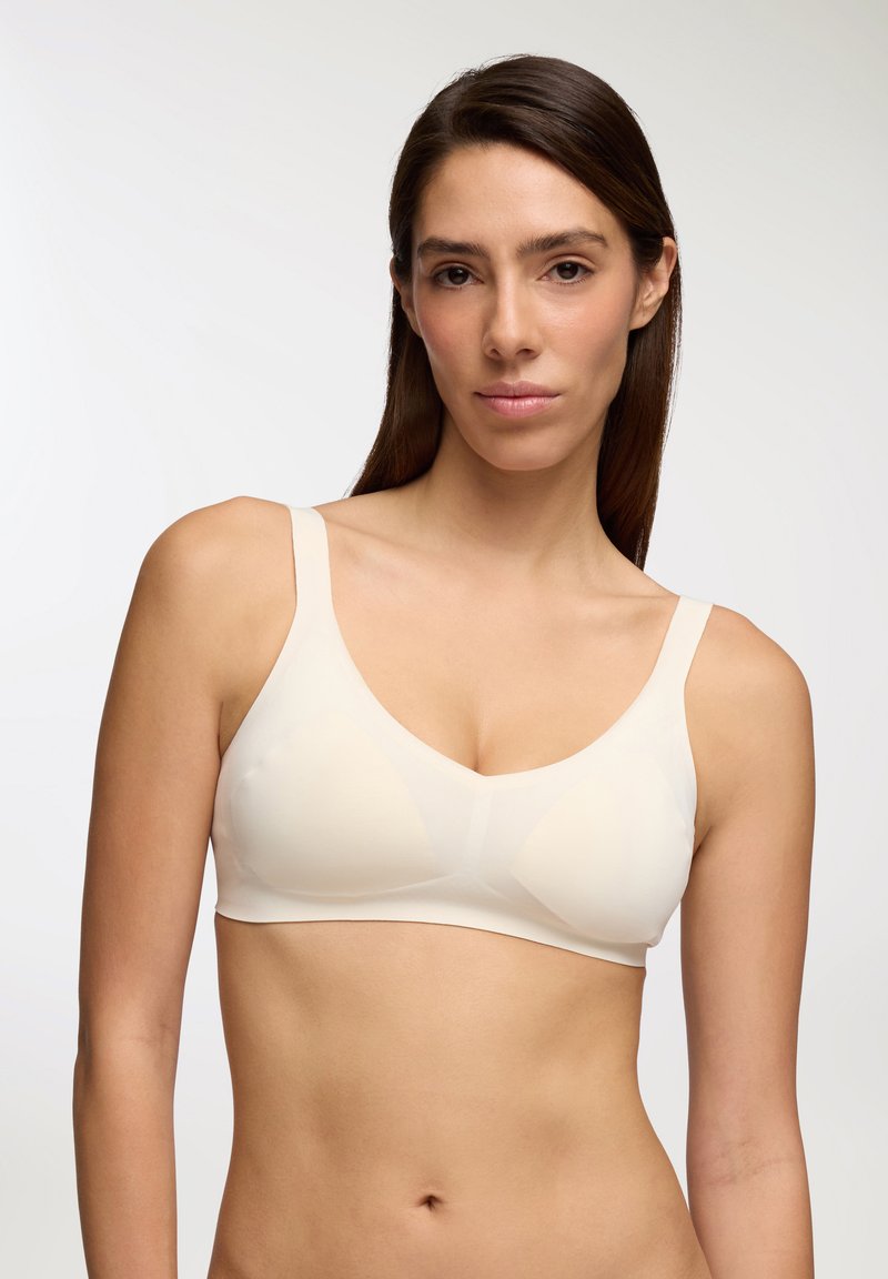Brassiere senza cuciture di un beige chiaro, con spalline larghe e scollatura a V. Tessuto liscio e elastico con minimo hardware e senza cuciture visibili.
