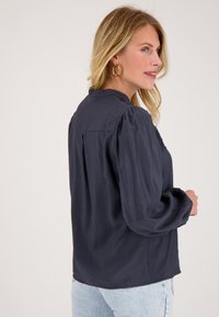 Donkerblauwe blouse met lange mouwen, een ontspannen pasvorm, ronde halslijn en gerimpelde schouders, met een getextureerd accent op het borstgebied.