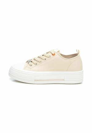 Zapatillas de lona beige con una suela de goma blanca, que presentan cinco ojetes metálicos y un pequeño acento naranja en el costado. Diseño de punta redonda.