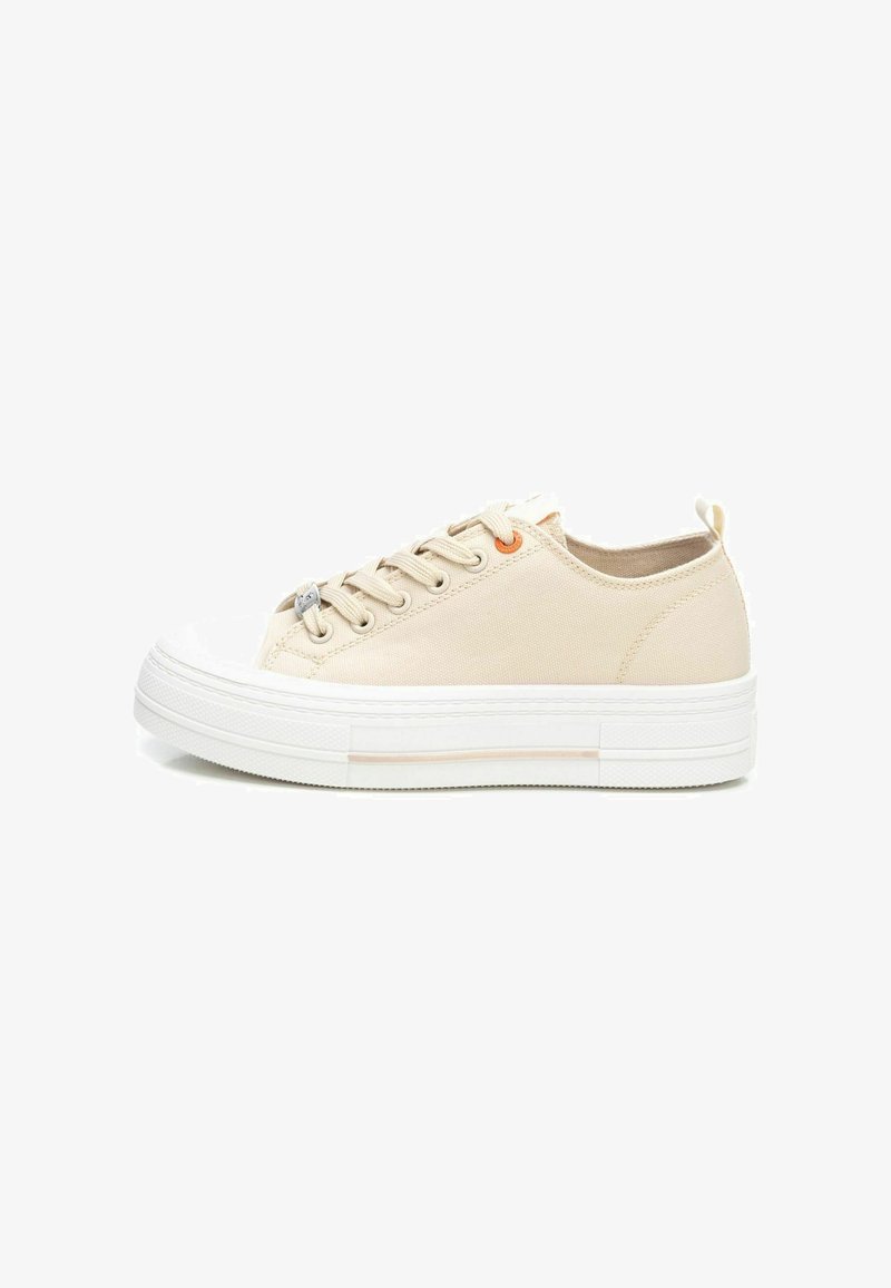 Zapatillas de lona beige con una suela de goma blanca, que presentan cinco ojetes metálicos y un pequeño acento naranja en el costado. Diseño de punta redonda.