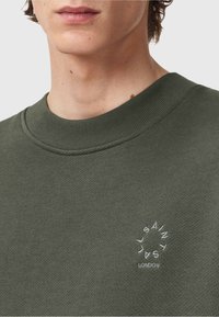 Felpa verde oliva con colletto a coste, caratterizzata da testo ricamato bianco in un design circolare sul petto. Texture morbida.