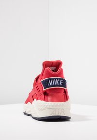 Röd Nike-sneaker med ovandel i tyg, marinblå detaljer, vadderad krage och en vit mellansula med struktur. Baksidan visar "NIKE" och "AIR"-märken.