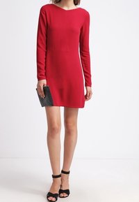 Punainen pitkähihaista mekkoa pyöreällä kaula-aukolla, istuvalla bodicella ja hieman laajenevalla hameella. Yhdistetty mustien nilkkaremmillisten sandaalien ja teksturoidun clutchin kanssa.