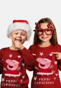 Maglioni di Natale rossi con un personaggio di maiale in un cappello di Babbo Natale, con il testo "BUON NATALE" e motivi a stella. Bambini che indossano accessori festivi.