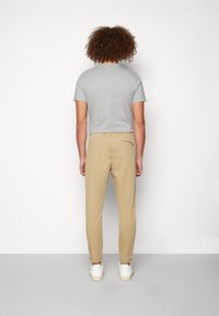 Graues kurzärmliges T-Shirt kombiniert mit beigen, schmal geschnittenen Hosen und weißen Sneakern. Die Hosen haben einen elastischen Bund und eine Gesäßtasche.