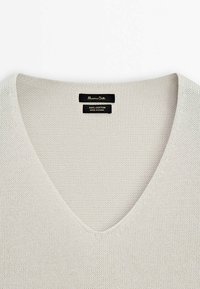 Pull gris clair en maille avec col en V, avec deux étiquettes noires indiquant la marque et les détails du tissu à l'intérieur de l'encolure.