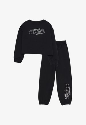 Felpa nera corta con testo bianco "DIMENSIONE danza sisters" e pantaloni felpati neri abbinati con lo stesso logo vicino alla caviglia.