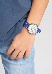 Montre pour enfants avec un bracelet en silicone bleu, boîtier rond en argent, cadran multicolore vibrant affichant les marques des heures et des minutes.