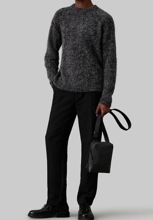 Šedý pletený svetr s texturovaným, chlupatým materiálem; kombinovaný s černými kalhotami na míru a černými koženými botami; drží malou černou kabelku.