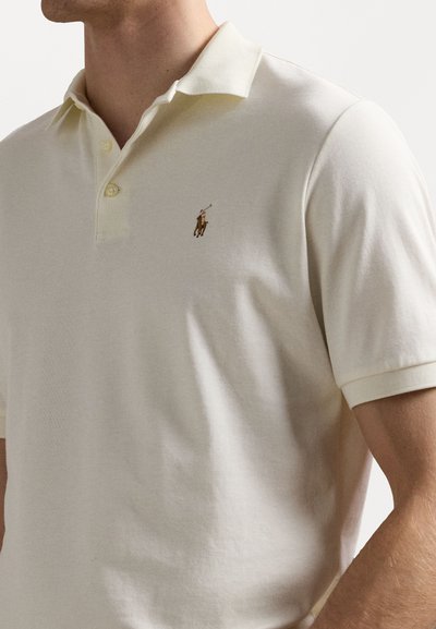 Koszulka polo w jasnokremowej bawełnie z klasycznym kołnierzykiem, dwoma guzikami i haftowanym logo na lewym piersi. Krótkie rękawy i gładka tekstura.