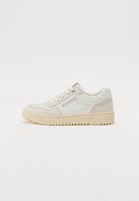 White and beige sneaker with leather and suede materials, rounded shape, textured sole, and lacing, featuring a logo on the side.