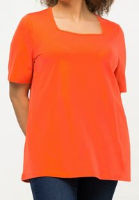 Camiseta de manga corta y escote cuadrado en naranja brillante, hecha de una tela suave con un corte relajado, combinada con jeans oscuros.