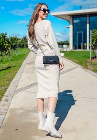 Light beige ribbed knit dress with a fitted silhouette, paired with white ankle boots. Black crossbody bag with a quilted design. Clear sky backdrop.
