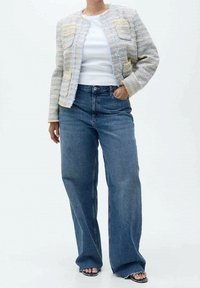 Veste en tweed bleu clair et beige avec bords effilochés, associée à un jean bleu à jambes larges et des sandales noires à bout ouvert.