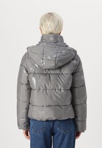 Grå puffjakke med hette, featuring en blank finish, quiltet design, og geometrisk mønster. Kombinert med blå denimjeans.