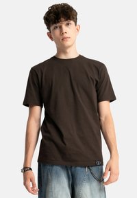 Brązowa bawełniana koszulka z krótkimi rękawami, okrągłym dekoltem i subtelną teksturą. Połączona z jasnymi dżinsami z akcentem w postaci łańcucha.