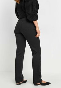 Svarta stretchjeans med rak benklipp, femfickorsdesign och synliga bakfickor. Matchade med svarta platta skor.