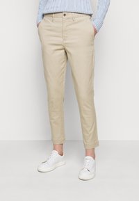 Bežové chinos kalhoty s rovnou nohavicí, s kapsami, knoflíkovým zapínáním a hladkým bavlněným materiálem. V kombinaci s bílými teniskami.