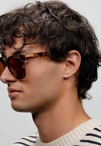 Sunglasses med sköldpadds-mönstrad ram, mörka linser och fyrkantig form. Glasögonen har minimala hårdvarudetaljer och texturerade kanter.