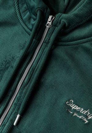 Groene geribde zip-up hoodie van zachte stof, met een zilveren rits en een geborduurd "Superdry" logo in het wit op de voorkant.