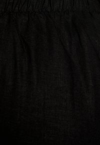 Svart tyg med en strukturerad yta, med ett plisserat midjeband. Materialet verkar lätt och något genomskinligt.