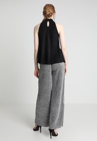 Svart plisserad halterneck-top med nyckelhål i ryggen, parat med silvermönstrade vida byxor. Båda plaggen har flödande, texturerad tyg.