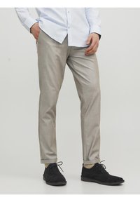 Pantaloni su misura grigio chiaro con una finitura liscia, vestibilità slim e pieghe sottili. Abbinati a scarpe in suede nere per un aspetto raffinato.