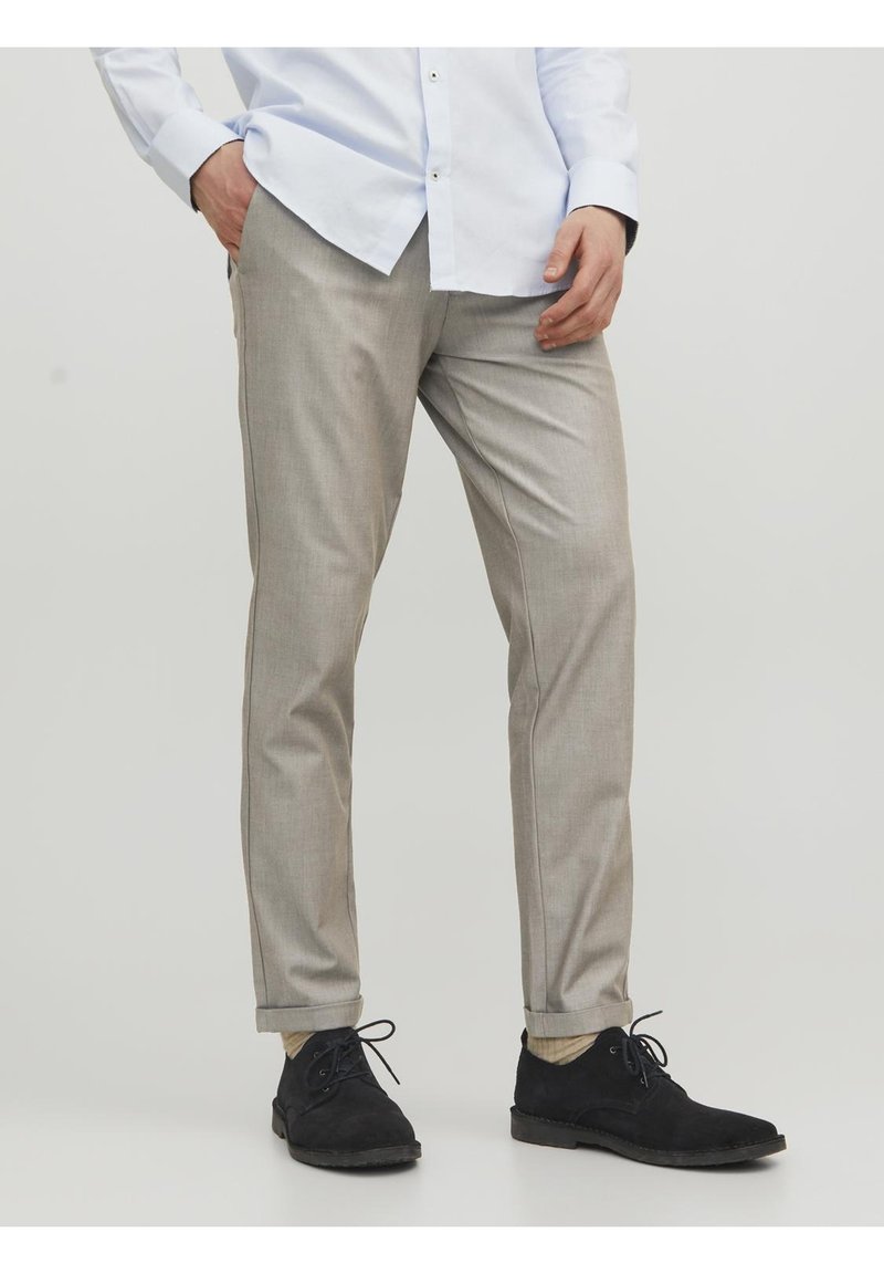 Pantaloni su misura grigio chiaro con una finitura liscia, vestibilità slim e pieghe sottili. Abbinati a scarpe in suede nere per un aspetto raffinato.