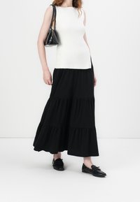 Witte mouwloze top met een geribbelde textuur, gecombineerd met een vloerlange zwarte gelaagde rok. Gecombineerd met een kleine zwarte tas en zwarte schoenen.