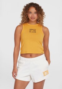 Cropped yellow tank top with black "WOMEN OF THE WAVE" graphic; paired with white elastic waist shorts featuring similar text in orange.