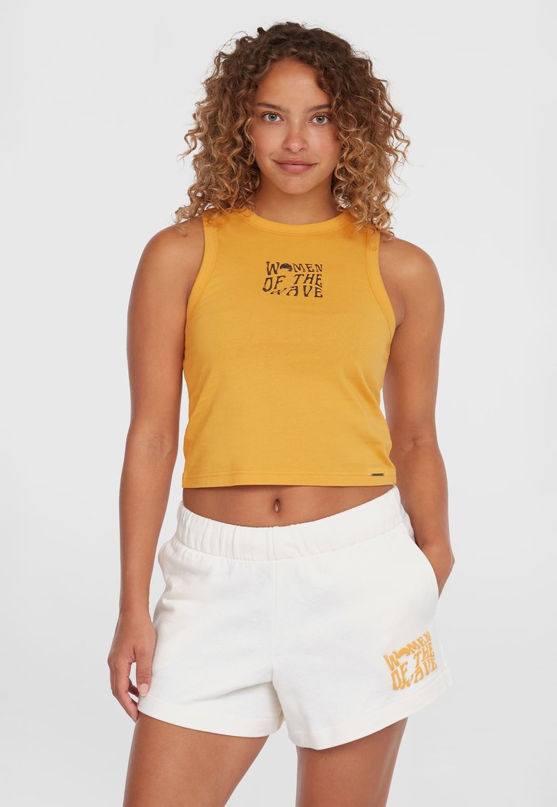 Cropped yellow tank top with black "WOMEN OF THE WAVE" graphic; paired with white elastic waist shorts featuring similar text in orange.