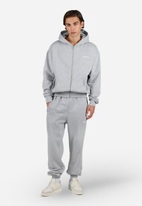 Gray zip-up hoodie and matching sweatpants made of soft fabric. Features ribbed cuffs, side pockets, and embroidered logo detail.