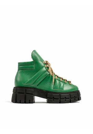 Groene leren enkellaarzen met dikke zwarte profielzool en beige veters, geregen door gouden oogjes, zijaanzicht op witte achtergrond.