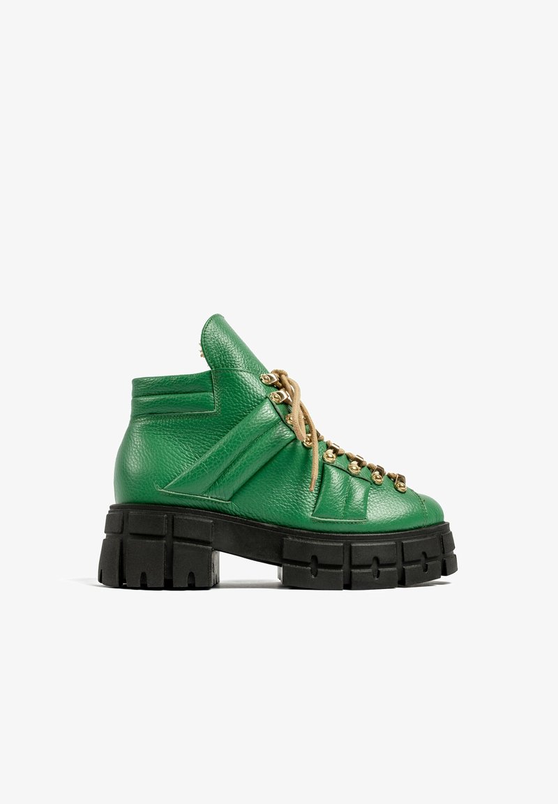 Bottine en cuir vert avec semelle noire crantée épaisse et lacets beige passés dans des œillets dorés, vue de côté sur fond blanc.