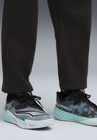 Adidași negri și albaștri cu un superior din plasă texturată, având o talpă teal și accente albe, concepuți pentru performanță și confort.